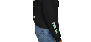 Side view of model wearing Sunday Club’s black crewneck sweatshirt with green “Sunday Club” graphic on sleeve. Athletic fit styled with denim for a casual game day look.